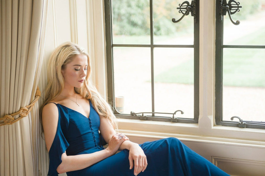 Woman with blonde hair sitting in a blue dress by the window