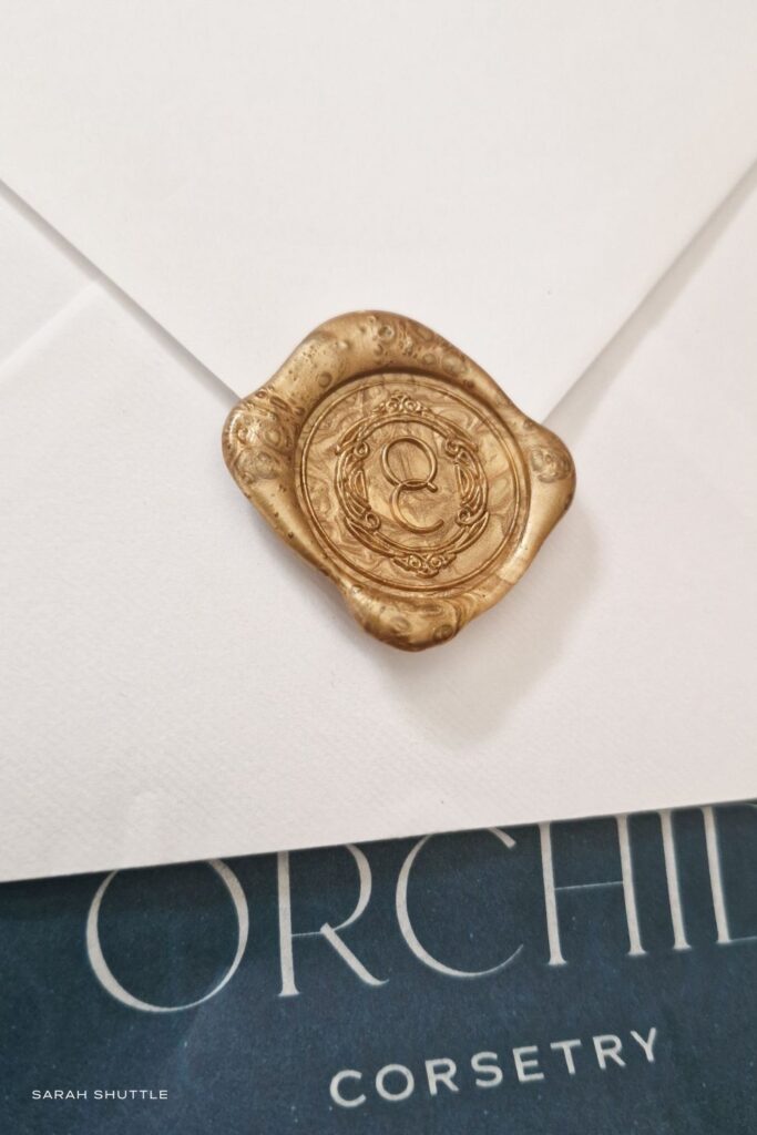 Ornate gold wax seal on white envelope with teal paper, created for a bespoke luxury corsetry brand.